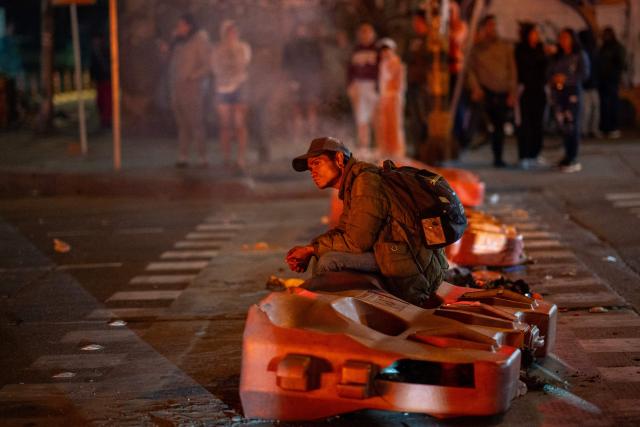 A demonstrator sits on collapsed plastic traffic barriers during clashes over the preliminary results of the presidential runoff election in Bogota, Colombia, on June 21, 2026. A flamboyant US-backed lawyer who has never held public office narrowly won Colombia's presidential runoff Sunday, swinging the country hard to the right on a promise to wage war against drug-running guerrilla groups. With more than 99 percent of polling centers reporting, Abelardo de la Espriella had 49.67 percent of the vote, an unassailable lead over his rival, left-wing Senator Ivan Cepeda who trailed at 48.69 percent, according to official results. (Photo by Diego Cuevas / AFP)