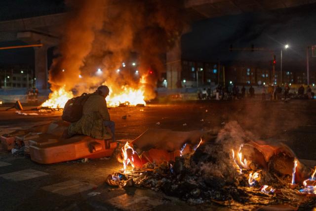 A demonstrators sits by burning barricades during clashes over the preliminary results of the presidential runoff election in Bogota, Colombia, on June 21, 2026. A flamboyant US-backed lawyer who has never held public office narrowly won Colombia's presidential runoff Sunday, swinging the country hard to the right on a promise to wage war against drug-running guerrilla groups. With more than 99 percent of polling centers reporting, Abelardo de la Espriella had 49.67 percent of the vote, an unassailable lead over his rival, left-wing Senator Ivan Cepeda who trailed at 48.69 percent, according to official results. (Photo by Diego Cuevas / AFP)