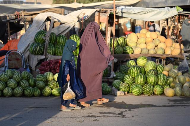 An Afghan burqa-clad woman along with a girl shops at a market in Merwais Mena town in Afghanistan's Kandahar on June 21, 2026. (Photo by Sanaullah SEIAM / AFP)