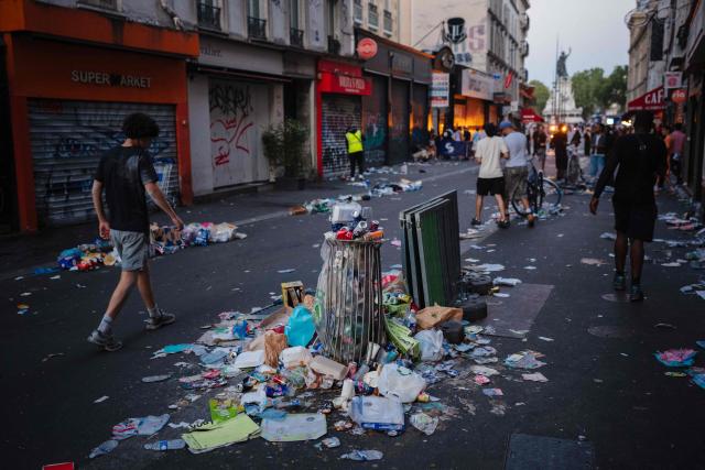 Pedestrians and partygoers walk past food and drink waste on a street with Le Monument à la République statue in the background on the morning following the national annual street music festival 'Fete de la Musique' in Paris on June 22, 2026. (Photo by DIMITAR DILKOFF / AFP)