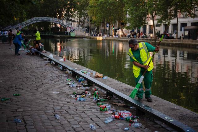 Municipal workers clean up food and drink waste on the banks of the Canal Saint-Martin in the background after the national annual street music festival 'Fete de la Musique' in Paris on June 22, 2026. (Photo by DIMITAR DILKOFF / AFP)