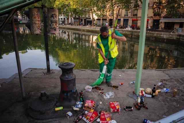 A municipal worker cleans up food and drink waste on the banks of the Canal Saint-Martin  on the morning following the national annual street music festival 'Fete de la Musique' in Paris on June 22, 2026. (Photo by DIMITAR DILKOFF / AFP)