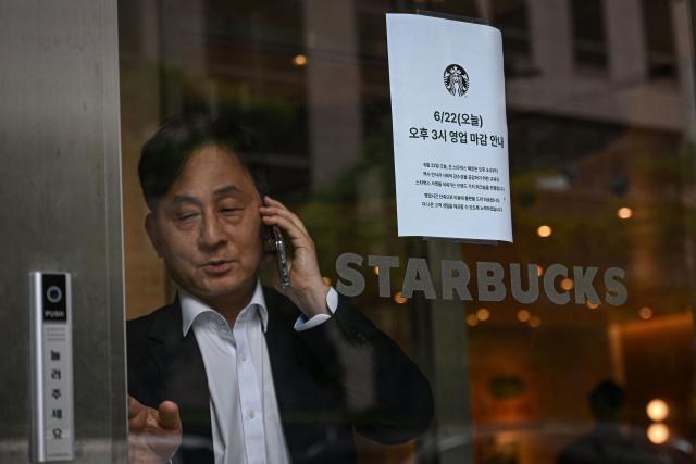 A man leaves a Starbucks coffee shop as an early closing notice is seen on the door in Seoul on June 22, 2026. Lights off. Doors closed. This was the scene across more than 2,000 Starbucks shops in South Korea on Monday afternoon, as all staff underwent "historical and social awareness" learning sessions in the wake of the "Tank Day" fiasco. (Photo by Jade GAO / AFP)