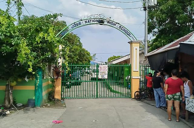 People stand next to the entrance gate of San Jose National High School after a shooting incident in Tacloban City, Leyte province on June 22, 2026. At least three teenaged students were killed and five others wounded on June 22, in a rare school shooting in the central Philippines, police said. (Photo by Noel  Sianosa / AFP)