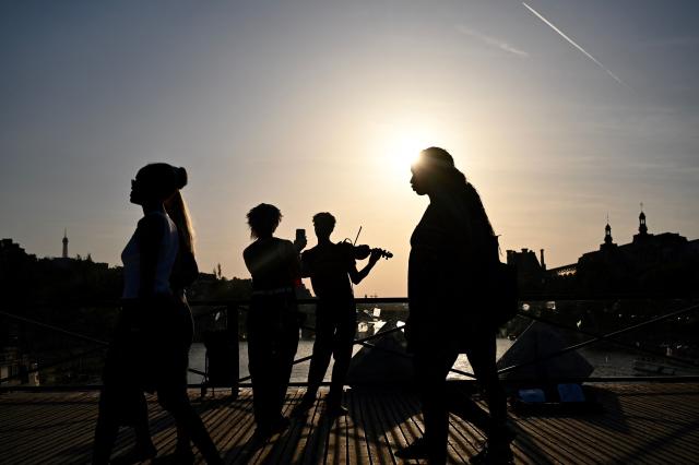 A violonist (C) plays under the sun on the Pont des Arts footbridge during the annual street music festival 'Fete de la Musique' and amid a heat wave in Paris on June 21, 2026. The Fete de la Musique (France's national music festival) was held on June 21, 2026, amid a the heatwave, with 35 departments under a red alert – a record number – where alcohol consumption will be banned. (Photo by Christophe DELATTRE / AFP)