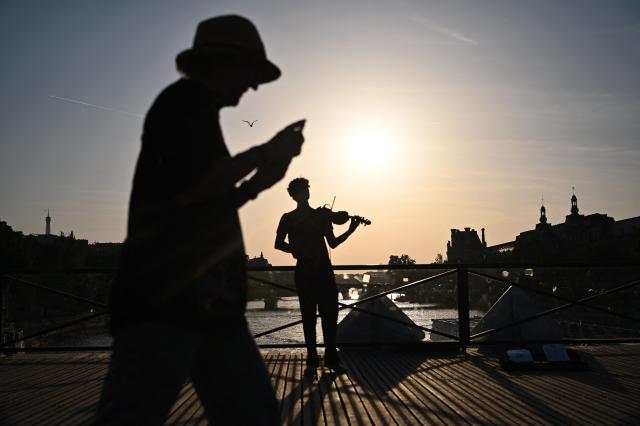 A violonist (C) plays under the sun on the Pont des Arts footbridge during the annual street music festival 'Fete de la Musique' and amid a heat wave in Paris on June 21, 2026. The Fete de la Musique (France's national music festival) was held on June 21, 2026, amid a the heatwave, with 35 departments under a red alert – a record number – where alcohol consumption will be banned. (Photo by Christophe DELATTRE / AFP)
