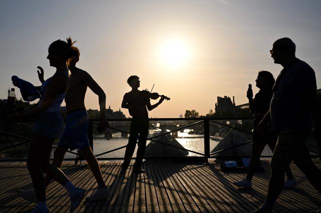 A violonist (C) plays under the sun on the Pont des Arts footbridge during the annual street music festival 'Fete de la Musique' and amid a heat wave in Paris on June 21, 2026. The Fete de la Musique (France's national music festival) was held on June 21, 2026, amid a the heatwave, with 35 departments under a red alert – a record number – where alcohol consumption will be banned. (Photo by Christophe DELATTRE / AFP)