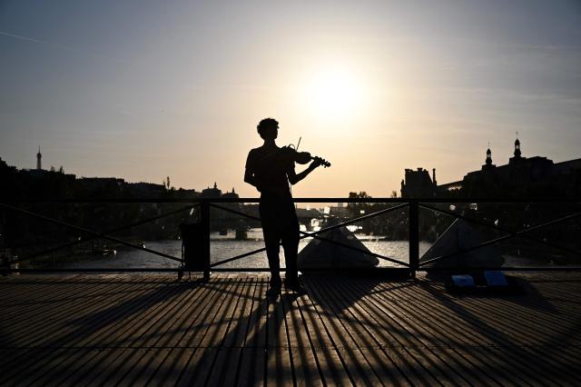 A violonist (C) plays under the sun on the Pont des Arts footbridge during the annual street music festival 'Fete de la Musique' and amid a heat wave in Paris on June 21, 2026. The Fete de la Musique (France's national music festival) was held on June 21, 2026, amid a the heatwave, with 35 departments under a red alert – a record number – where alcohol consumption will be banned. (Photo by Christophe DELATTRE / AFP)