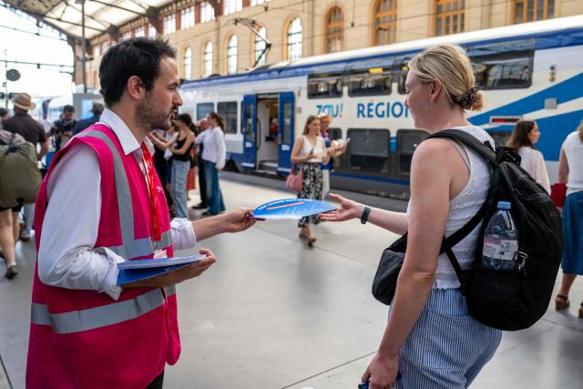A staff member hands out fans to customers as part of a distribution of water bottles, hats and fans organised by the Region Sud - Provence Alpes Cote d'Azur region at the Saint-Charles railway station in Marseille on June 22, 2026, as a heatwave hits France. France was set on June 22, 2026 to experience the hottest day yet in its latest heatwave after a sweltering night, with a peak of 43C expected in the southwest. In a first, France's highest heat warning was issued across half the country for June 22, 2026, with forecasters warning the extreme weather episode could end up being as serious as a 2003 heatwave that claimed the lives of nearly 15,000 people nationwide. (Photo by Miguel MEDINA / AFP)