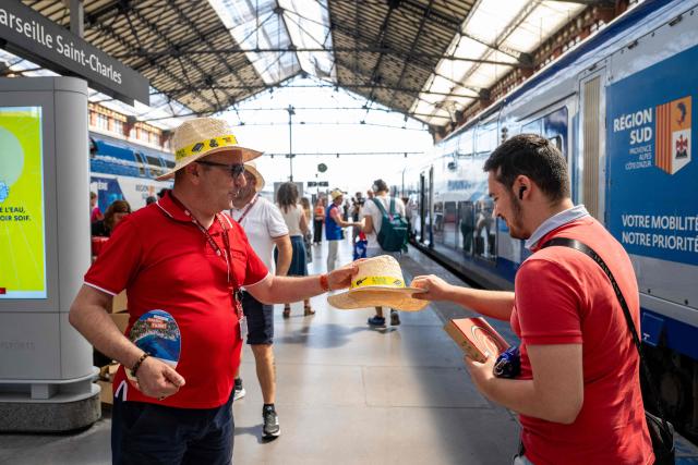 A staff member hands out hats to customers as part of a distribution of water bottles, hats and fans organised by the Region Sud - Provence Alpes Cote d'Azur region at the Saint-Charles railway station in Marseille on June 22, 2026, as a heatwave hits France. France was set on June 22, 2026 to experience the hottest day yet in its latest heatwave after a sweltering night, with a peak of 43C expected in the southwest. In a first, France's highest heat warning was issued across half the country for June 22, 2026, with forecasters warning the extreme weather episode could end up being as serious as a 2003 heatwave that claimed the lives of nearly 15,000 people nationwide. (Photo by Miguel MEDINA / AFP)
