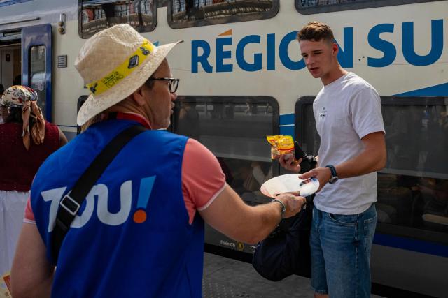 A staff member hands out fans to customers as part of a distribution of water bottles, hats and fans organised by the Region Sud - Provence Alpes Cote d'Azur region at the Saint-Charles railway station in Marseille on June 22, 2026, as a heatwave hits France. France was set on June 22, 2026 to experience the hottest day yet in its latest heatwave after a sweltering night, with a peak of 43C expected in the southwest. In a first, France's highest heat warning was issued across half the country for June 22, 2026, with forecasters warning the extreme weather episode could end up being as serious as a 2003 heatwave that claimed the lives of nearly 15,000 people nationwide. (Photo by Miguel MEDINA / AFP)