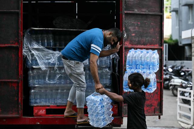 Workers unload packaged drinking water bottles from a truck at a distribution point in Bengaluru on June 22, 2026. (Photo by Idrees MOHAMMED / AFP)