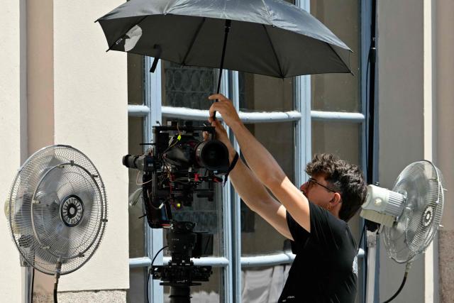 A technician protects his camera from the heat with an umbrella before the Thom Browne collection show at Milan's Fashion Week Menswear Spring/Summer 2027, in Milan on June 22, 2026. (Photo by Stefano RELLANDINI / AFP)