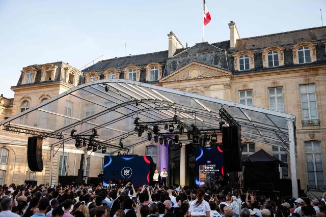 France's President Emmanuel Macron (R), acccompanied by his wife Brigitte Macron addresses attendees during the annual street music festival 'Fete de la Musique' and amid a heat wave at the Presidential Elysee Palace in Paris on June 21, 2026. (Photo by Yoan VALAT / POOL / AFP)