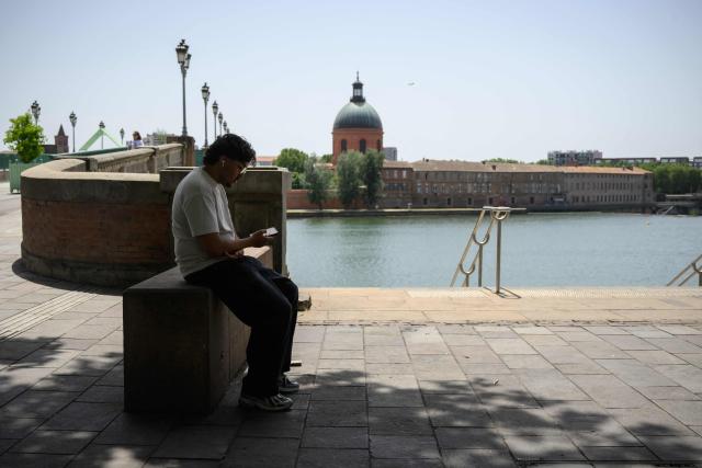 A man sits in the shade before the Garonne river in Toulouse during a heatwave on June 22, 2026. (Photo by Ed JONES / AFP)