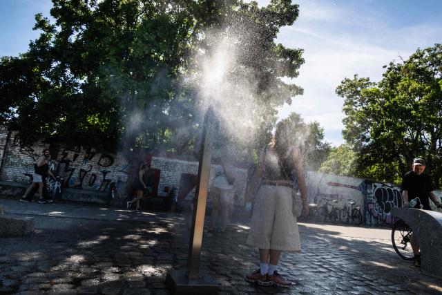 A woman cools off at a mist spraying fountain, known as a "cooling point", in Berlin on June 22, 2026. (Photo by John MACDOUGALL / AFP)