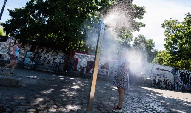 A woman cools off at a mist spraying fountain, known as a "cooling point", in Berlin on June 22, 2026. (Photo by John MACDOUGALL / AFP)
