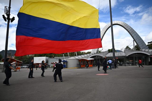 Employees hoist a Colombian national flag outside Corferias, the largest polling center in the country, during the vote count, the day after the presidential election runoff, in Bogota on June 22, 2026. Rightist leaders from across the Americas congratulated Colombia's hard-right president-elect Abelardo de la Espriella after he defeated his leftist rival in a razor-tight vote on June 21, 2026. With almost all the votes counted, De la Espriella held 49.66 percent of the ballots versus Senator Ivan Cepeda's 48.70 percent. (Photo by Raul ARBOLEDA / AFP)