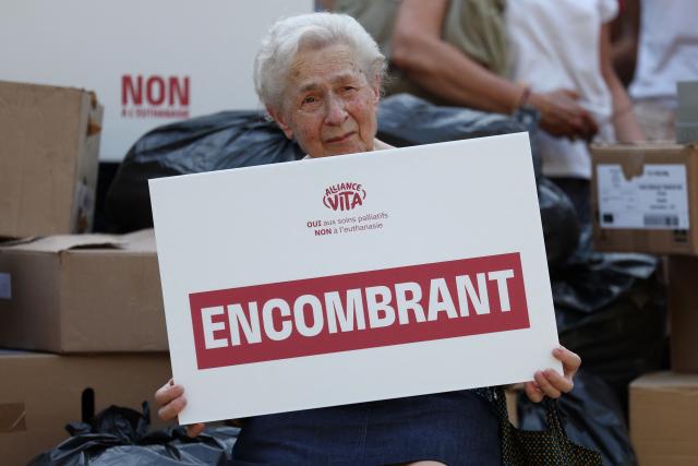 A protester sits with a placard that reads "Burden" during a rally organised by French "pro-life" organisation Alliance Vita against the new French draft law on euthanasia and assisted suicide at Invalides, in Paris on June 22, 2026.  (Photo by Charlotte SIEMON / AFP)