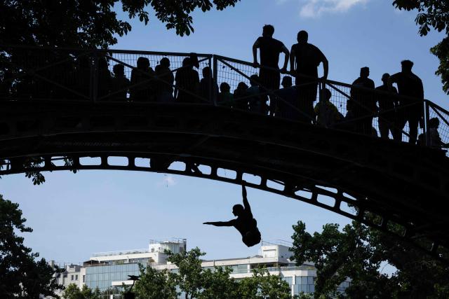 Young people jump from a bridge into the Canal Saint-Martin during a heatwave in Paris on June 22, 2026. Due to the ongoing heatwave sweeping across France - the Bassin des Recollets - a portion of the Canal Saint-Martin in the French capital has been opened for swimming from June 17. (Photo by JOEL SAGET / AFP)