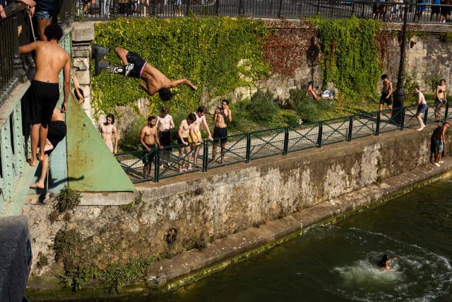 Swimmers jump from a bridge into the Canal Saint-Martin as France experiences a heatwave, in Paris on June 22, 2026. Due to the ongoing heatwave sweeping across France - the Bassin des Recollets - a portion of the Canal Saint-Martin in the French capital has been opened for swimming from June 17. (Photo by JOEL SAGET / AFP)