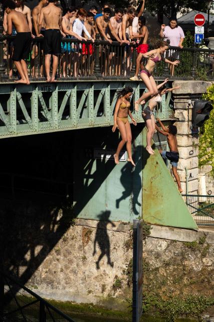 Swimmers jump from a bridge into the Canal Saint-Martin as France experiences a heatwave, in Paris on June 22, 2026. Due to the ongoing heatwave sweeping across France - the Bassin des Recollets - a portion of the Canal Saint-Martin in the French capital has been opened for swimming from June 17. (Photo by Joel Saget / AFP)