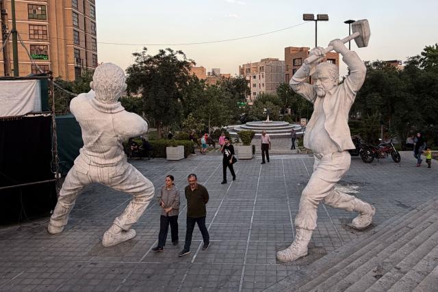 Iranian walks between sculptures of workers in Tehran on June 22, 2026. The United States temporarily suspended sanctions on Iranian oil on June 22 after Vice President JD Vance said Iran would allow UN nuclear inspectors to return to the country, following talks in Switzerland. (Photo by ATTA KENARE / AFP) / 