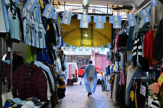 An fan wrapped in an Argentinian national flag walks at a market during the 2026 FIFA World Cup football match between Argentina and Austria in Buenos Aires on June 22, 2026. (Photo by Luis ROBAYO / AFP)