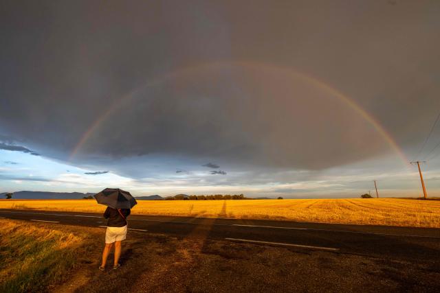A woman takes a photograph of a rainbow in Valensole, southern France, on June 22, 2026. (Photo by Miguel MEDINA / AFP)