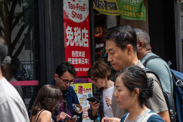 Tourists check their phones outside a tax free shop in Tokyo on June 23, 2026, as the weak yen continues to draw foreign shoppers. The yen, weighed down in particular by the prospect of monetary tightening by the US Federal Reserve (Fed), approached its lowest level in 40 years. If it falls below 161.95 yen, it will drop to levels not seen since December 1986. (Photo by Andrew CABALLERO-REYNOLDS / AFP)