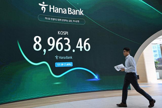 A currency dealer walks past a screen showing South Korea's benchmark stock index (KOSPI) in a foreign exchange dealing room at the Hana Bank headquarters in Seoul on June 23, 2026. (Photo by Jade GAO / AFP)