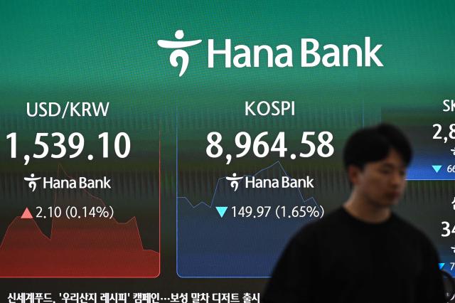 A currency dealer walks in front of an electronic screen showing South Korea's benchmark stock index (R) and the Korean won/USD exchange rate (L) in a foreign exchange dealing room at the Hana Bank headquarters in Seoul on June 23, 2026. (Photo by Jade GAO / AFP)