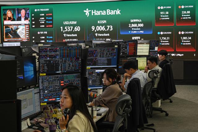 Currency dealers monitor exchange rates as a screen shows South Korea's benchmark stock index (KOSPI) in a foreign exchange dealing room at the Hana Bank headquarters in Seoul on June 23, 2026. (Photo by Jade GAO / AFP)