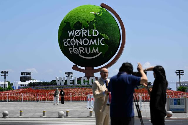 A flower installation and globe with the logo of the World Economic Forum is pictured outside the Dalian International Conference Centre during the World Economic Forum Annual Meeting of the New Champions in Dalian, China's Liaoning province, on June 23, 2026. (Photo by WANG Zhao / AFP)