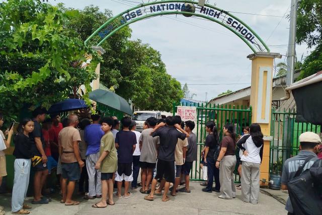 Students and their parents wait for permission from school authorities to enter the school compound at the gate of San Jose High School in Tacloban City, Leyte province in the central Philippines on June 23, 2026, a day after a shooting incident. Two students opened fire June 22 inside a school in the central Philippines, a rare campus shooting that killed three teens and wounded seven others, police said. (Photo by Noel  Sianosa / AFP)