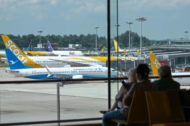 Passenger aircraft including a Xiamen Air Boeing 737 Max 8 (front L) is seen as people look on from a viewing gallery at the Singapore Changi Airport in Singapore on June 23, 2026. (Photo by Roslan RAHMAN / AFP)