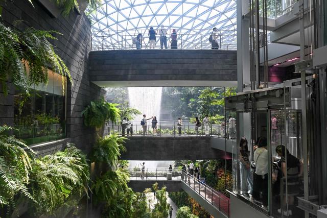 People take pictures from the bridge next to the Rain Vortex, the world's tallest indoor waterfall, at the Jewel Complex at Singapore Changi Airport in Singapore on June 23, 2026. (Photo by Roslan RAHMAN / AFP)
