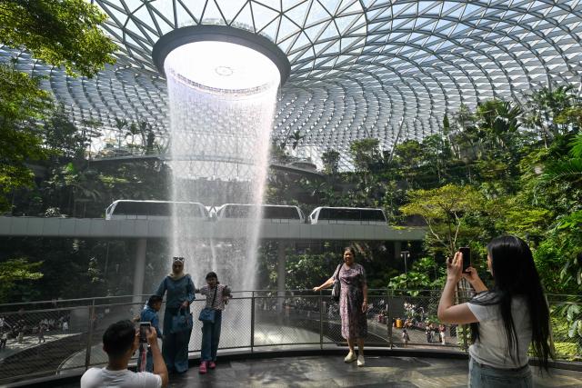 People take pictures against the Rain Vortex, the world's tallest indoor waterfall, at the Jewel Complex at Singapore Changi Airport in Singapore on June 23, 2026. (Photo by Roslan RAHMAN / AFP)