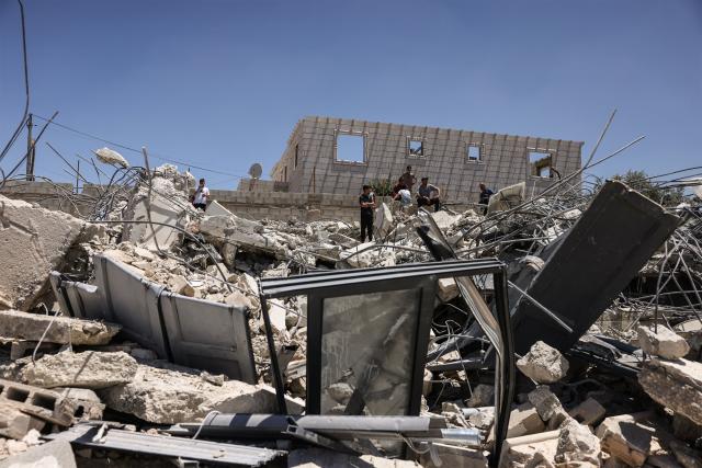 Palestinians climb on the rubble after Israeli bulldozers guarded by Israeli soldiers demolish the home and shops belonging to the Palestinian al-Atrash family, citing the lack of a building permit, in the village of Qilqes, a few kilometres from the Israeli settlement of Beit Hagai, just south of the Israeli-occupied West Bank city of Hebron on June 23, 2026. Excluding east Jerusalem, which was occupied and annexed by Israel in 1967, some 500,000 Israeli settlers live in the West Bank, along with about three million Palestinian residents. (Photo by HAZEM BADER / AFP) / 