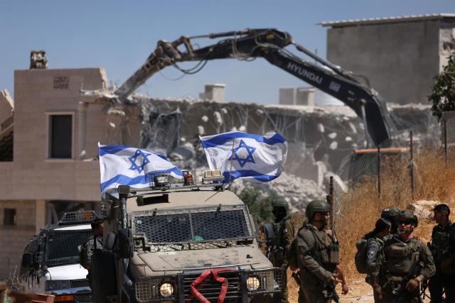 Israeli bulldozers guarded by Israeli soldiers demolish the home belonging to the Palestinian al-Atrash family, citing the lack of a building permit, in the village of Qilqes, a few kilometres from the Israeli settlement of Beit Hagai, just south of the Israeli-occupied West Bank city of Hebron on June 23, 2026. Excluding east Jerusalem, which was occupied and annexed by Israel in 1967, some 500,000 Israeli settlers live in the West Bank, along with about three million Palestinian residents. (Photo by HAZEM BADER / AFP) / 