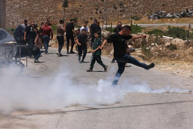 A Palestinian kicks away a teargas cyclinder fired by Israeli security forces guarding bulldozers demolishing the home and shops belonging to the al-Atrash family, citing the lack of a building permit in the village of Qilqes, a few kilometres from the Israeli settlement of Beit Hagai, just south of the Israeli-occupied West Bank city of Hebron on June 23, 2026. Excluding east Jerusalem, which was occupied and annexed by Israel in 1967, some 500,000 Israeli settlers live in the West Bank, along with about three million Palestinian residents. (Photo by HAZEM BADER / AFP)