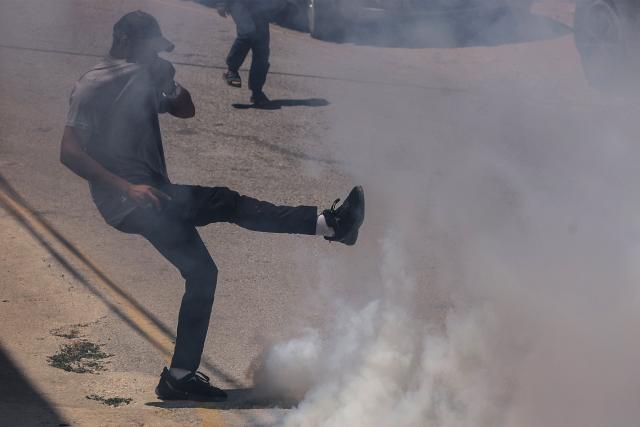A Palestinian kicks away a teargas cyclinder fired by Israeli security forces guarding bulldozers demolishing the home and shops belonging to the al-Atrash family, citing the lack of a building permit in the village of Qilqes, a few kilometres from the Israeli settlement of Beit Hagai, just south of the Israeli-occupied West Bank city of Hebron on June 23, 2026. Excluding east Jerusalem, which was occupied and annexed by Israel in 1967, some 500,000 Israeli settlers live in the West Bank, along with about three million Palestinian residents. (Photo by HAZEM BADER / AFP)