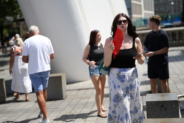 A person uses a fan to cool themselves from the heat, on a hot summer's day, in London on June 23, 2026. (Photo by Toby Shepheard / AFP)