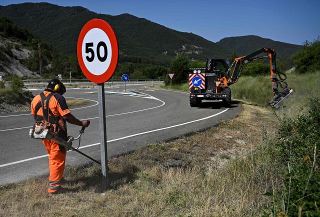 A worker cuts the grass on the side of the road in the Sobrarbe region, Huesca province, on June 23, 2026. Nearly all of Spain was under a heat alert on June 23, with parts of the south and north of the country placed on the highest warning level as a heatwave grips most of western Europe. Temperatures of up to 40C in the shade were forecast in parts of the Basque Country on the border with France, an area where such extreme heat is relatively uncommon. (Photo by ANDER GILLENEA / AFP)