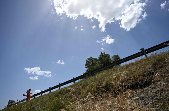 A worker cuts the grass on the side of the road in the Sobrarbe region, Huesca province, on June 23, 2026. Nearly all of Spain was under a heat alert on June 23, with parts of the south and north of the country placed on the highest warning level as a heatwave grips most of western Europe. Temperatures of up to 40C in the shade were forecast in parts of the Basque Country on the border with France, an area where such extreme heat is relatively uncommon. (Photo by ANDER GILLENEA / AFP)