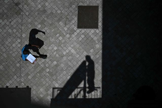 TOPSHOT - A pedestrian holds a clipboard as he walks past the shadow of a worker installing a placard at the bottom of a hotel in Bordeaux, southwestern France on June 23, 2026, as France experiences a heatwave. (Photo by Christophe ARCHAMBAULT / AFP)