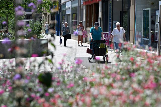 A person uses a mobility walker as they stroll through the high street in Huddersfield in northern England on June 23, 2026. Multiple schools in England shut early on June 23 and set to remain closed for two more days with a heatwave expected to set new records in the UK as it spreads across Europe. (Photo by Oli SCARFF / AFP)
