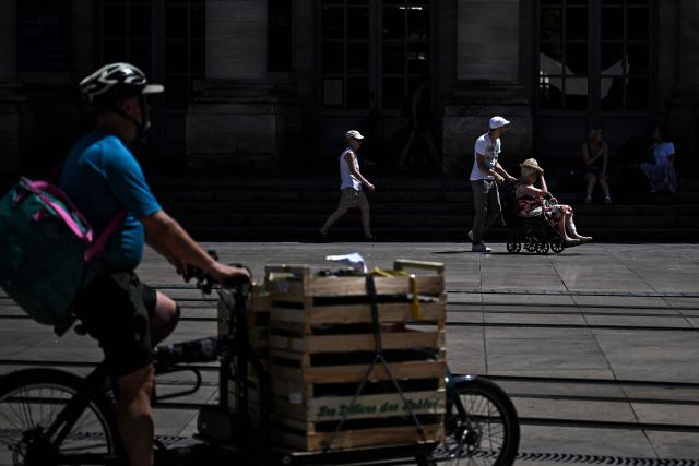 A cyclist rides past a pedestrian pushing a person in a wheelchair in Bordeaux, southwestern France on June 23, 2026, as France experiences a heatwave. (Photo by Christophe ARCHAMBAULT / AFP)
