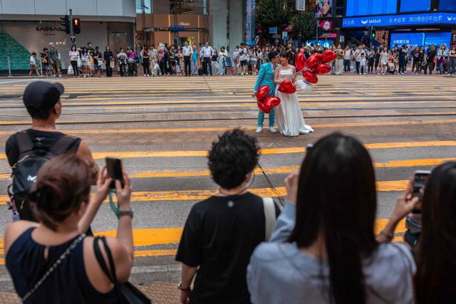 Pedestrians watch as a couple pose for pre-wedding photos on a street in Hong Kong on June 23, 2026. (Photo by Dale DE LA REY / AFP)