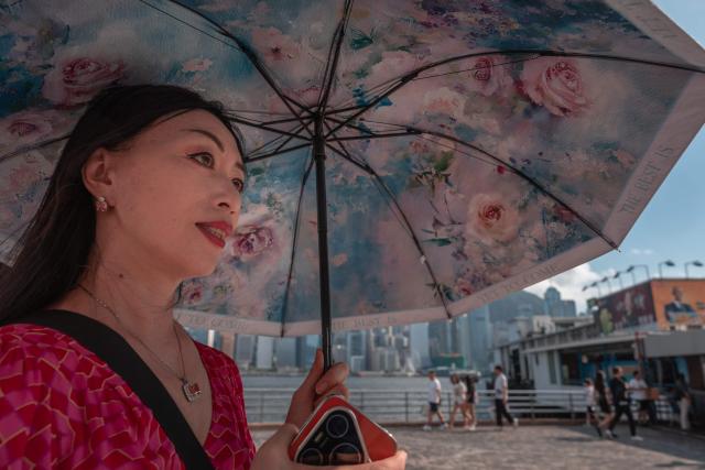 A tourist from mainland China uses an umbrella to block the sun while visiting a promenade along Victoria Harbour in Hong Kong on June 22, 2026. (Photo by Dale DE LA REY / AFP)